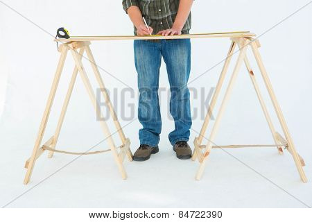 Low section of construction worker marking wooden table against white background