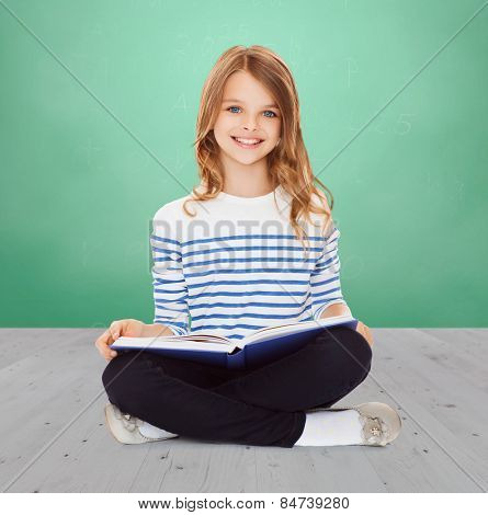education, childhood, people and school concept - little student girl studying and reading book over green chalk board background