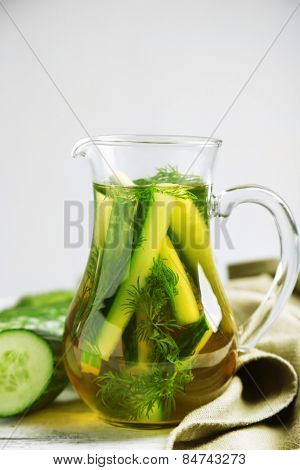Glass ewer with fresh organic cucumber water on wooden table, on grey background