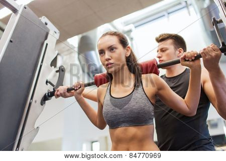 sport, fitness, teamwork, weightlifting and people concept - young woman and personal trainer with barbell flexing muscles in gym