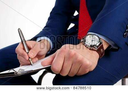 Businessman with a clock on the hand writes the document.