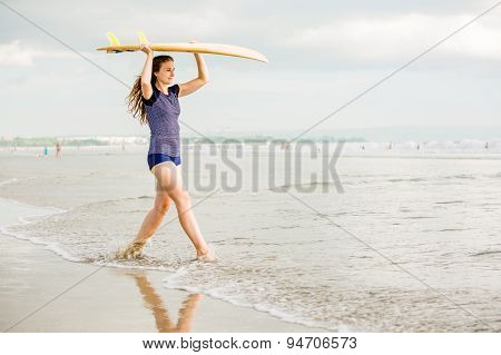 Beautiful sexy surfer girl on the beach at sunset walks along ocean shore, yellow surfboard in her h