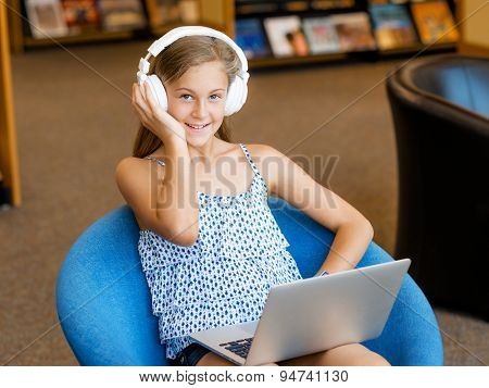A teenage girl with headphones sitting in a library
