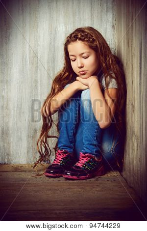 Portrait of a sad girl child sitting in the corner of the room. Loneliness, depression. Awkward age.