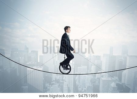 Brave guy riding a monocycle on a rope above cityscape concept