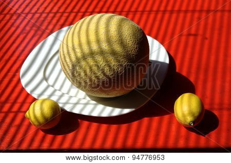 Cubist background with whole sugar melon on plate with two lemons.