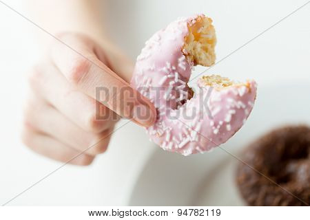 people, food, junk-food and eating concept - close up of female hand holding bitten glazed donut