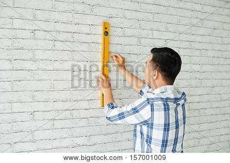 Young man measuring wall with level, vire from the back