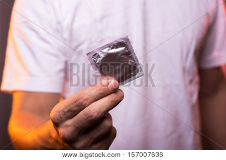 Unknown man in white shirt holding condom in hand closeup. Safety sex concept.