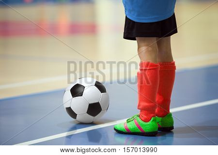 Football futsal training for children. Indoor soccer young player with a soccer ball in a sports hall. Player in blue and red uniform. Sport background.