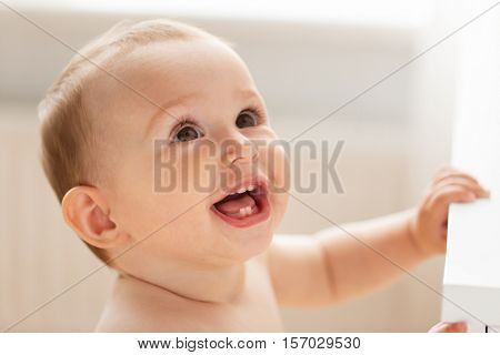 childhood, babyhood, emotions and people concept - close up of happy little baby boy or girl at home looking up