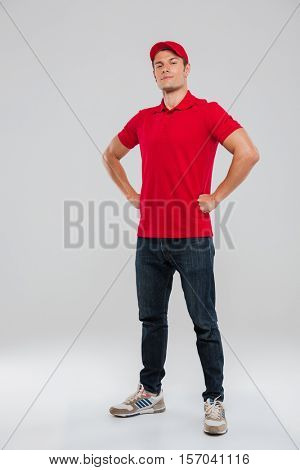 Full length portrait of deliveryman. arms akimbo. looking at camera. in studio. isolated gray background