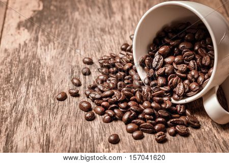 Spilled of coffee beans in white cup on wooden table