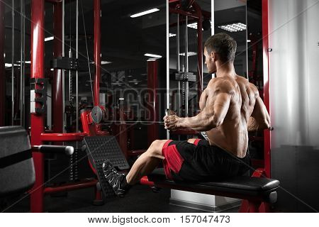 Athlete muscular bodybuilder training back on simulator in the gym. Sportly strong man douing exsercice.