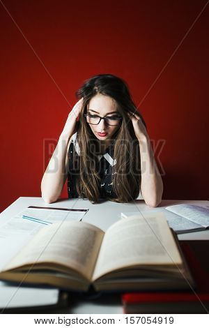 Young attractive brunette tired girl in glasses studying with book