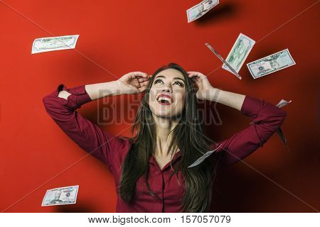 Attractive brunette woman with falling dollars banknotes red background, jackpot concept