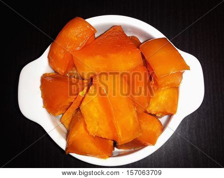 Slices of pumpkin with sugar baked in the oven. The white plate on a black background