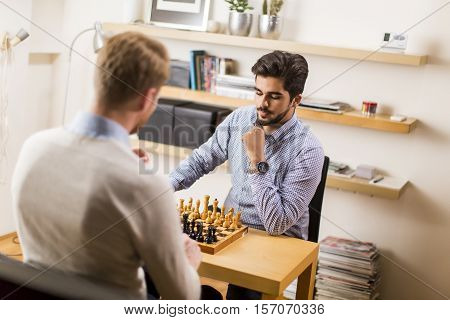 Two young men playing chess in room