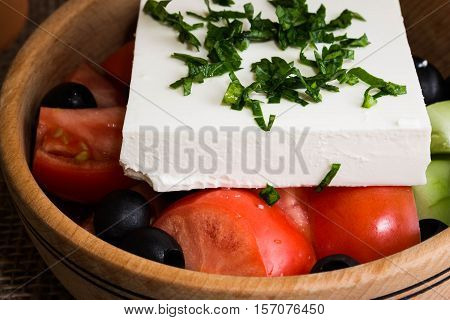 Greek salad with feta cheese and vegetables on wooden plate