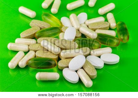 Mixed natural food supplement pills omega 3 calcium multivitamin and glucosamine capsules on green background