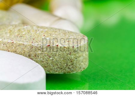 Mixed natural food supplement pills multivitamin tablet calcium and glucosamine capsules on green background macro image