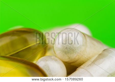 Mixed natural food supplement pills omega 3 and glucosamine capsules on green background