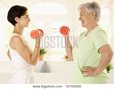 健康高齢者女性笑顔パーソナル トレーナー自宅、ダンベル運動を行うします?。