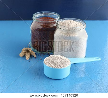 Healthy food ragi, or finger millet, flour, which is used in some Indian cuisines, in a measuring cup, and in the background are two bottles one with ragi and another with ragi flour.
