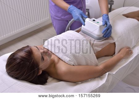 Pretty young woman getting cryolipolyse treatment in cosmetic cabinet