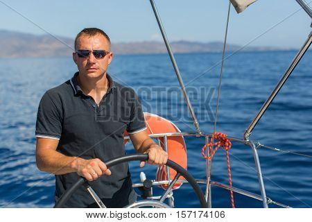 Male skipper at the helm sailing boat, controls ship during sea yacht race. Luxery vacations, adventure, travel.