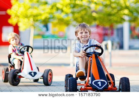 Two active little kid boys driving pedal race cars in summer outdoors. Children, best friends racing with fast speed and having fun. Twins making competition