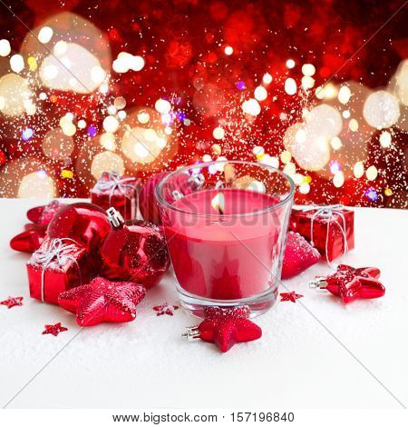 christmas red burning candle with christmas decorations on snow, red background with stras and bokeh lights