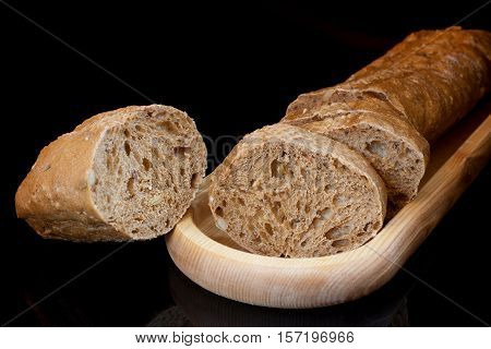 Close-up fresh sliced baguette on wooden oblong plate and sliced crust on black background.