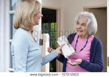 Mature Woman Delivering Newspaper To Elderly Neighbour