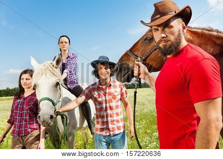 Portrait of young people and their beautiful horses in flowery meadow at sunny day