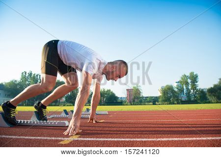 Male athlete on starting position at athletics running track. Runner practicing his sprint start in athletics stadium racetrack.