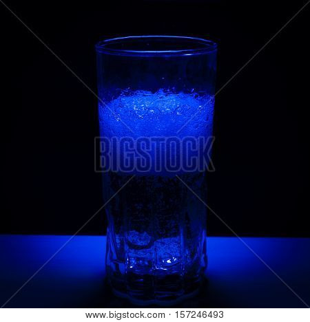 A half full drink with bubbles in blue light and dark bakground