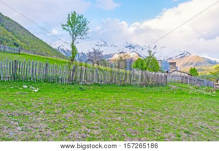 The rural view with the old wooden fence green pastures and the snowy mountains on background Mestia Upper Svaneti Georgia.