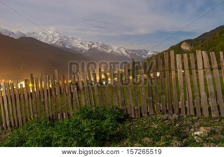 The old wooden fence hides eveninglights of Mestia Georgia.