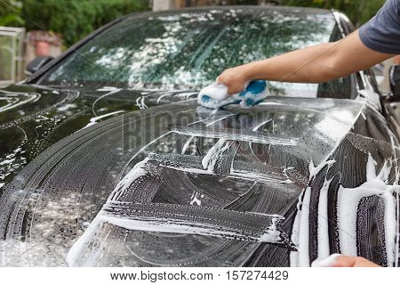 Car detailing series : Closeup of hand cleaning black car of serviceman.