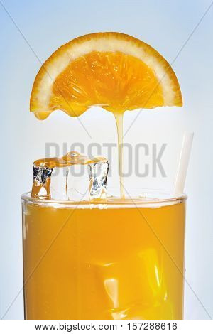 Orange juice is flowing in a glass with ice