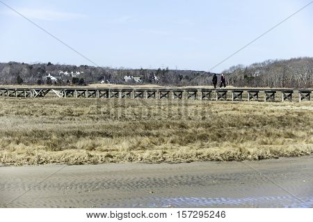 Sandwich Massachusetts USA - March 17 2010: Late winter morning with two women strolling along boardwalk over marsh at Sandwich Town Beach in Sandwich Massachusetts