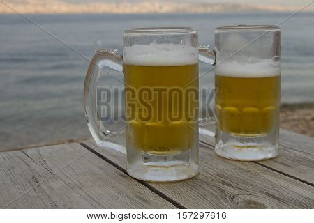 Thw glasses of beer on the wooden table near sea
