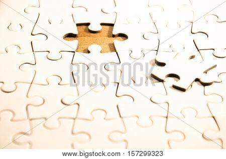 white jigsaw/puzzle whit one gap over a wooden table background the last piece is just close to the gap symbol of problem solving