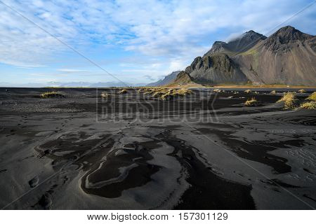 Mountains and black volcanic lava sand dunes by the sea in summer of Stokksness Iceland