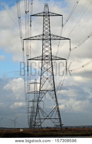 Stright row of electrical power pylons with a wind turbine in the back ground