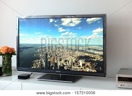 PARIS FRANCE - NOV 21 2015: Apple TV device next to 4k Pansonic Plasma OLED display projecting the typical Apple Screensaver of aerial city