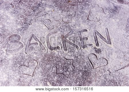 Baking (Backen) in German letters written in flour on the table