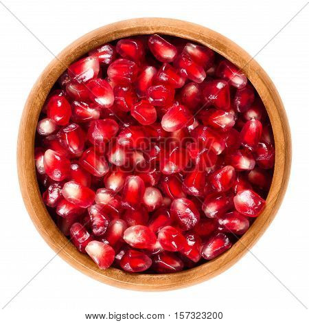 Fresh pomegranate seeds in wooden bowl. Edible red seeds from the fruit of Punica granatum, separated from the peel. Isolated macro food photo close up from above on white background.