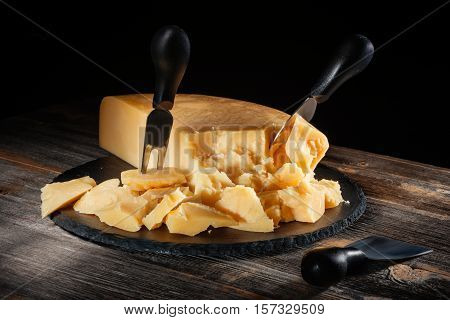 Cheese parmesan with a set of knives on a black round slate board in style a rustic
